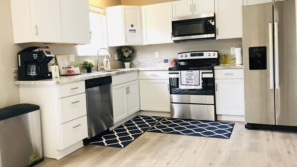 Una cocina moderna con armarios blancos, electrodomésticos de acero inoxidable y un tapete con estampado blanco y negro.