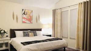 Un dormitorio con una cama, una mesita de noche, una lámpara, una ventana con cortinas y un cuadro en la pared.