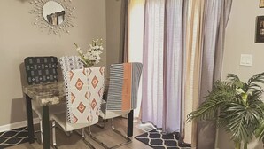 Una sala de estar con sofá, una mesita de noche con un florero, un espejo y una ventana con cortinas.