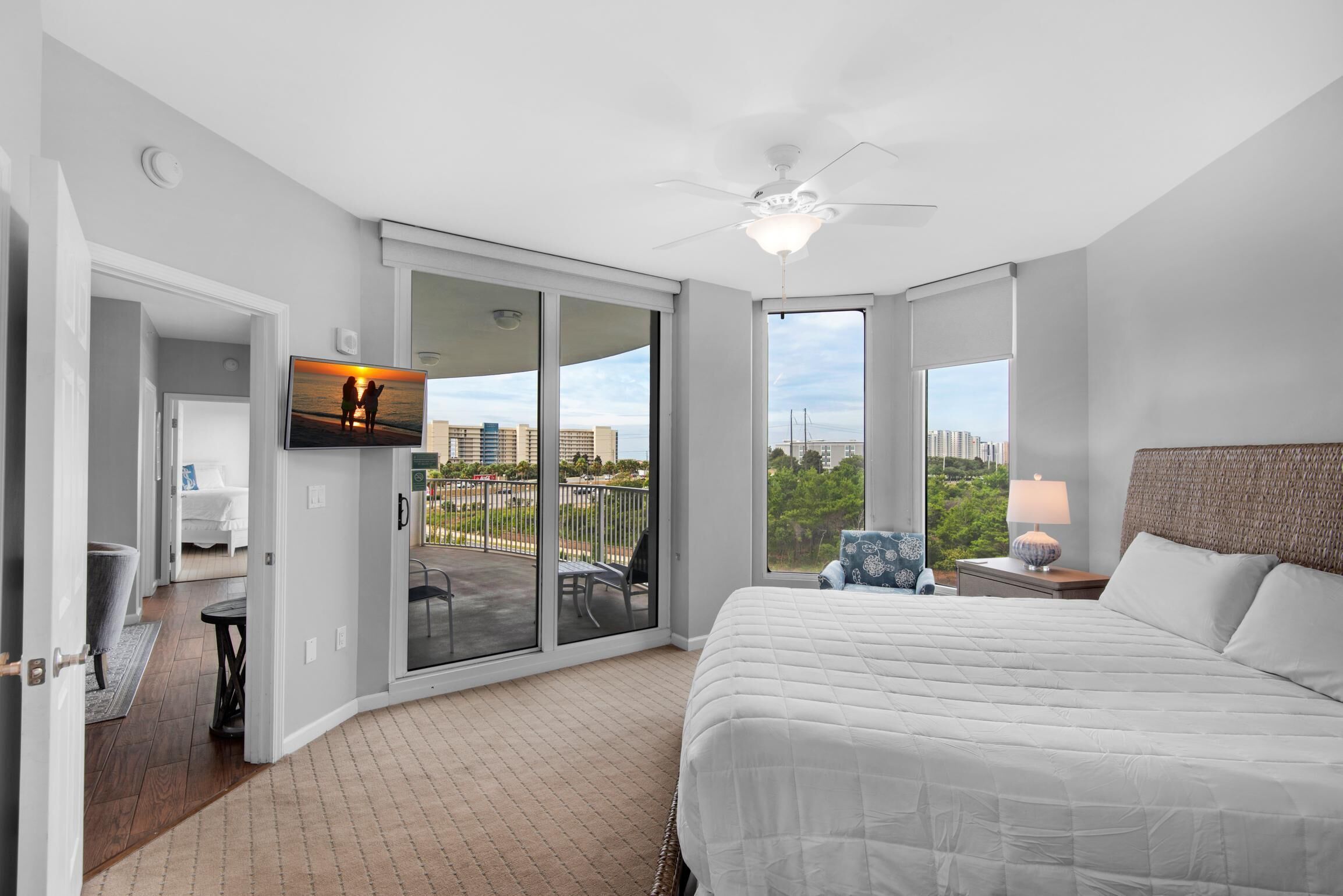 Une chambre d’hôtel avec un grand lit, un ventilateur de plafond, un téléviseur fixé au mur et un balcon offrant une vue sur la ville.