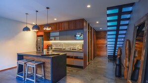 A modern kitchen with a central island, bar stools, pendant lighting, and a large window.