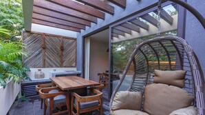 A patio with a wooden table and chairs, a wicker chair, and a view through a glass door.