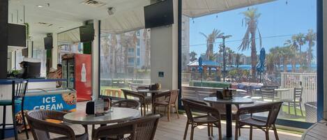 Een restaurant met rieten meubels, een Coca-Cola koelkast en uitzicht op een zwembad.