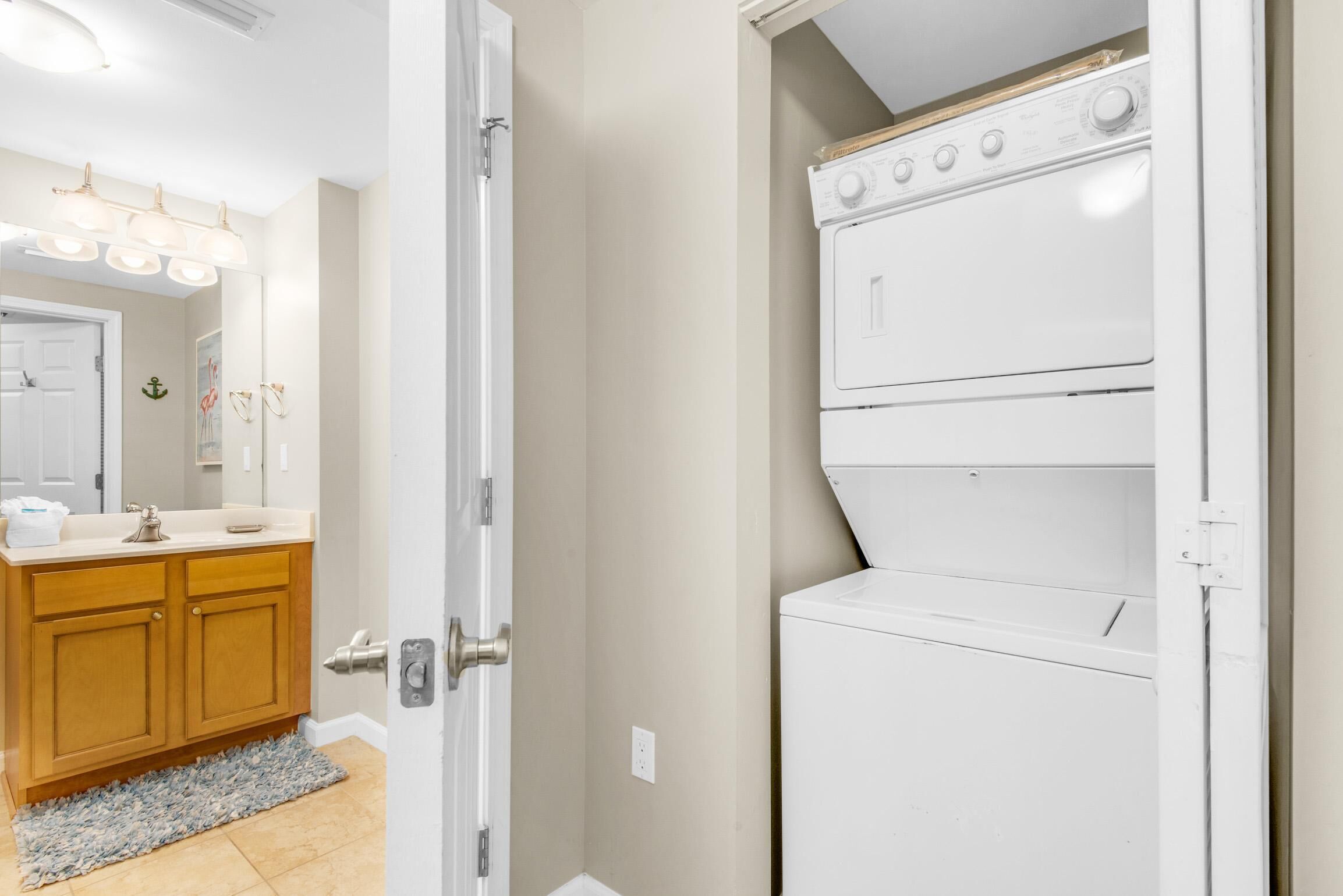 A laundry room with a white washer and dryer, wooden cabinets, and a mirror with lights above the sink.