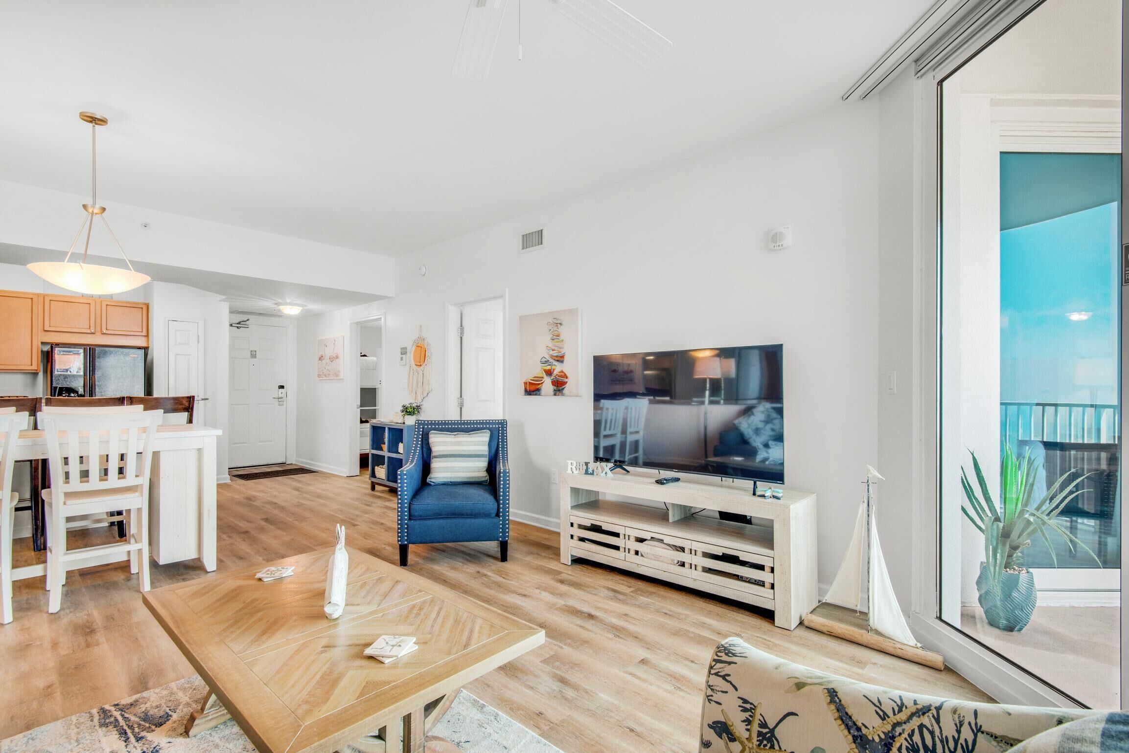 A modern living room with a wooden floor, white furniture, a television, and a large window with a view.