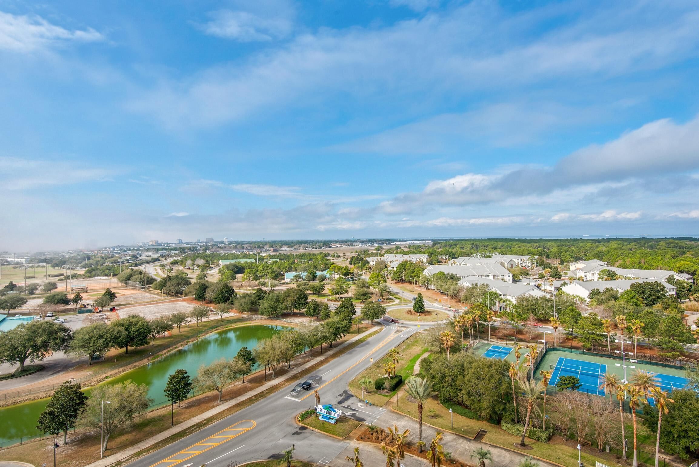 An aerial view of a residential area with a tennis court, a swimming pool, and a road with a traffic sign.