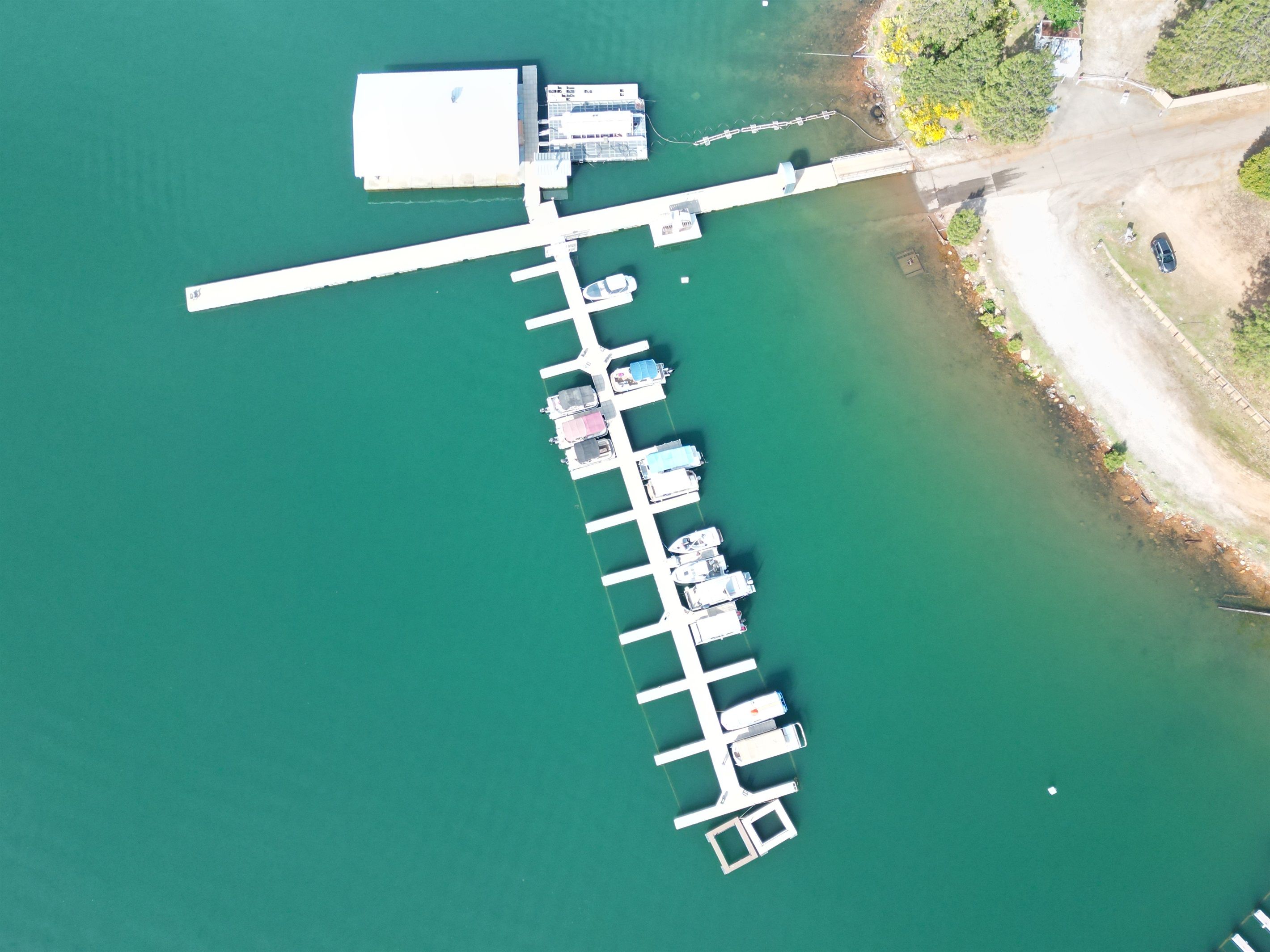 An aerial view of a dock with multiple boats, a large white building, and a clear green water body.