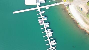 An aerial view of a dock with multiple boats, a large white building, and a clear green water body.