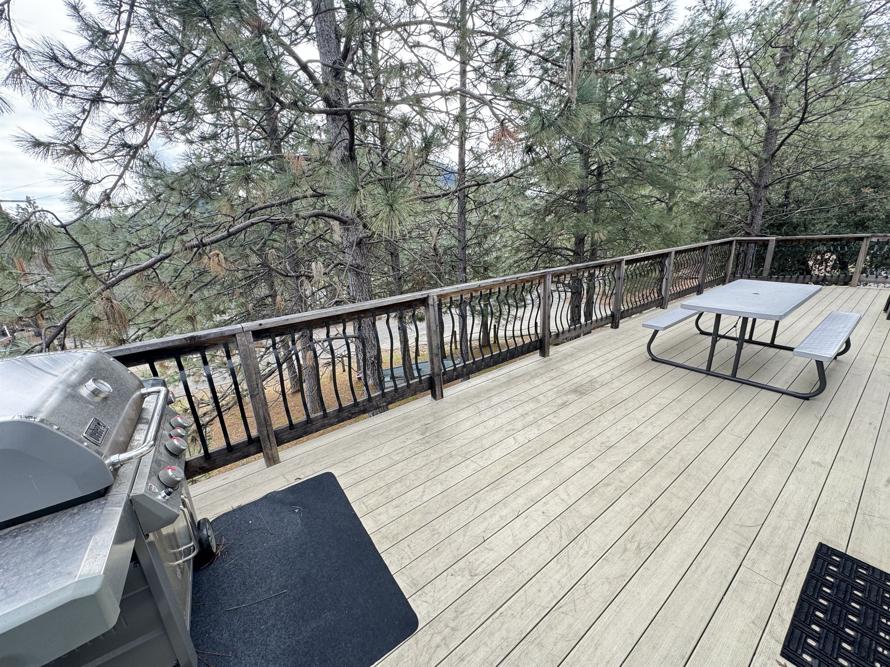 A deck with a grill, picnic table, and benches, surrounded by trees.