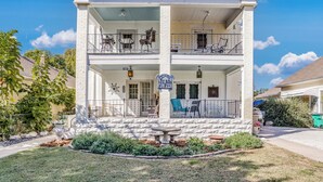 A two-story building with a balcony on the upper floor, a front porch with outdoor seating, and a well-maintained garden. - Travel Nurse Landing in Delano! W&D In Unit (Wichita)