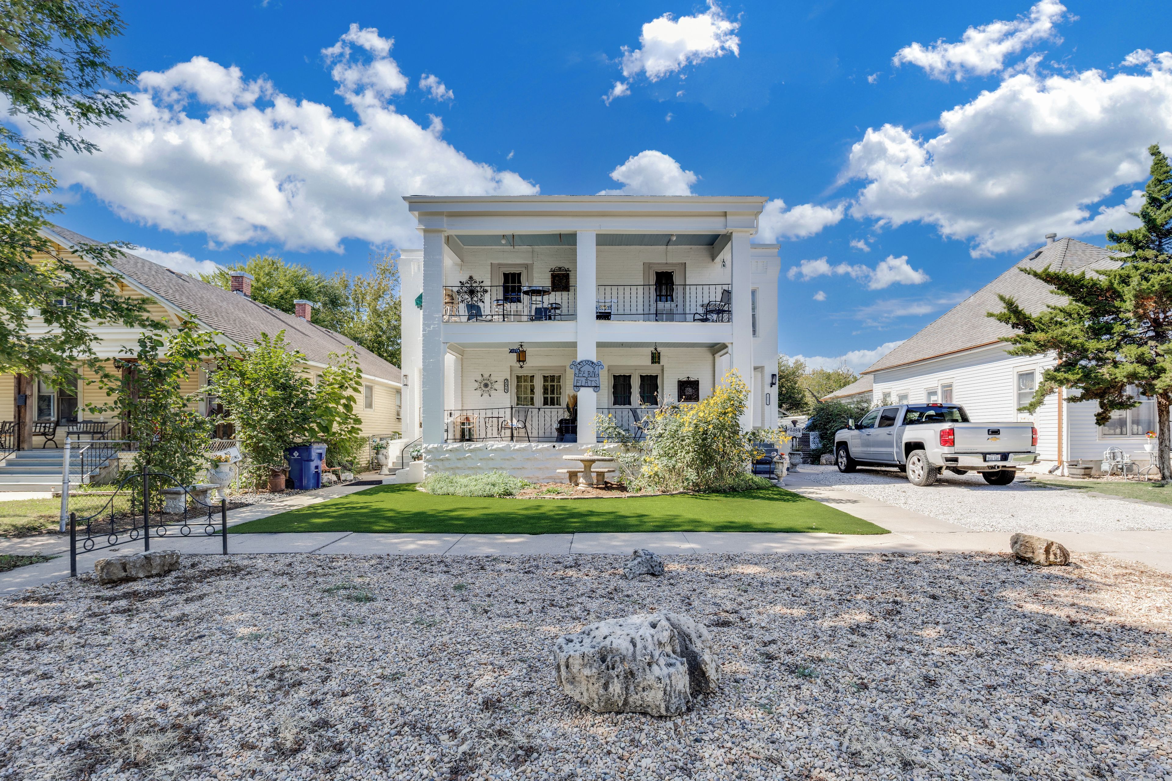 A two-story building with a balcony, a gravel driveway, and a parked truck.