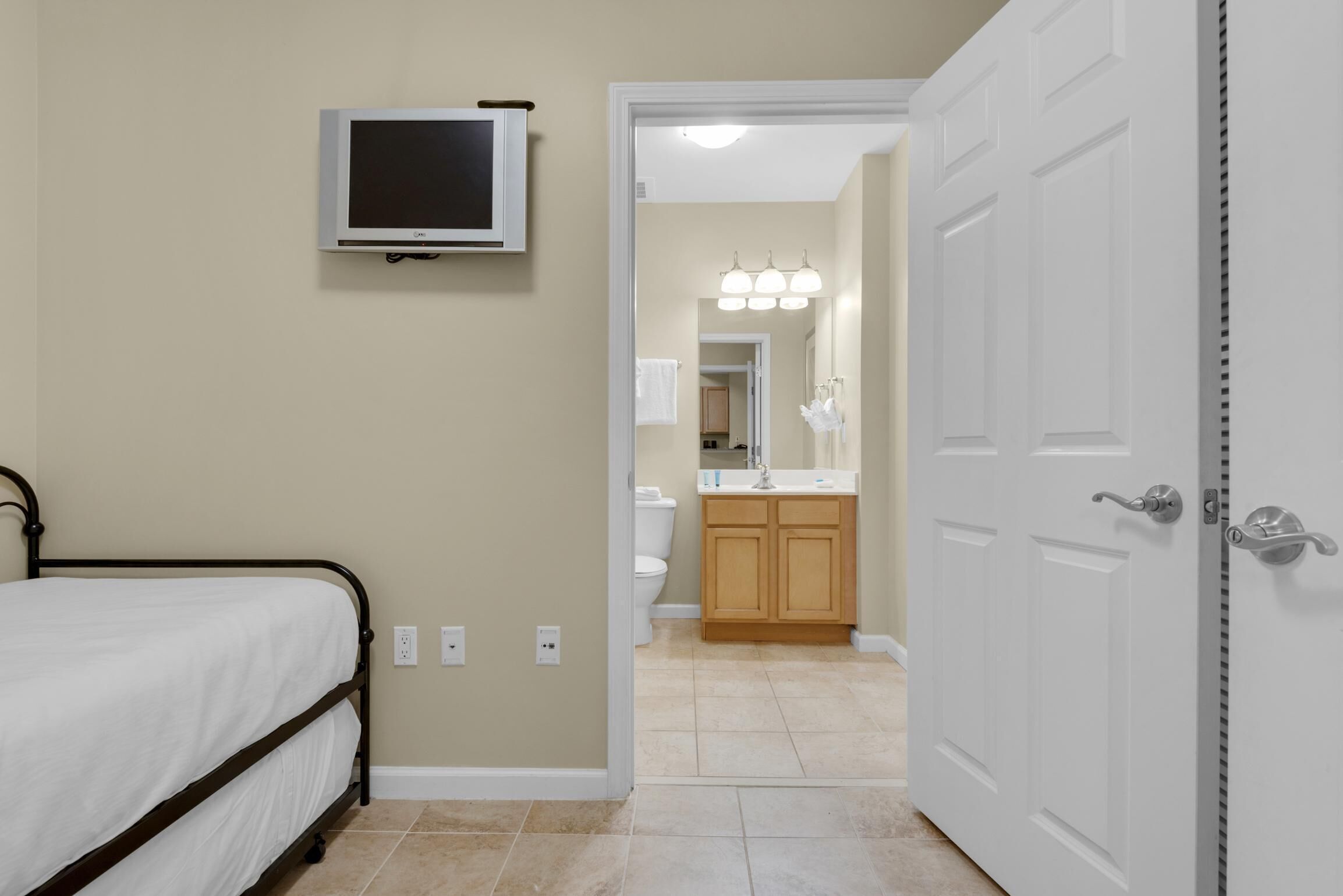 A bedroom with a bed, a television mounted on the wall, and a bathroom visible through an open door.