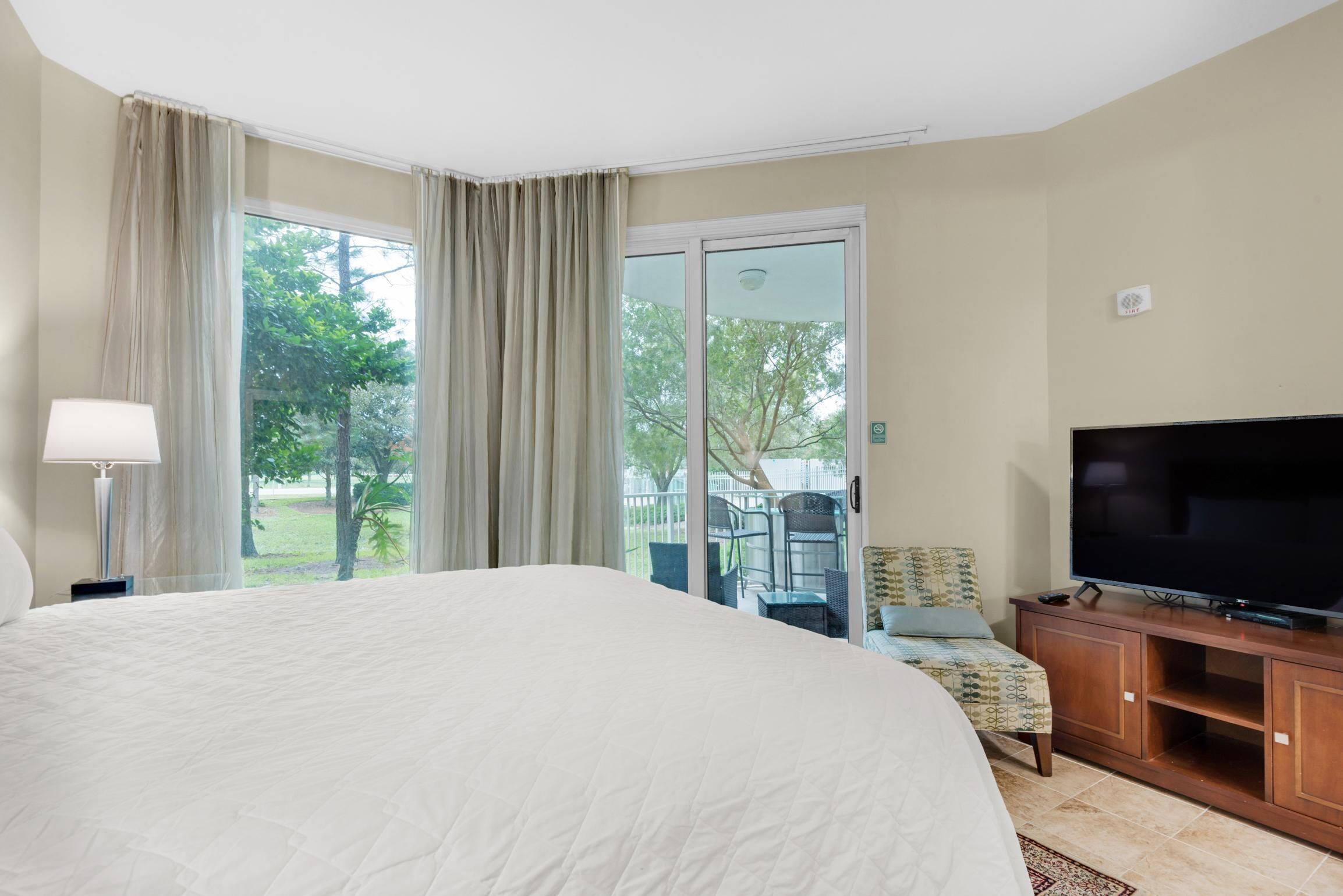 A hotel room with a large bed, a TV, a desk, and a view of the outdoors through a sliding glass door.