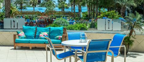 An outdoor seating area with a turquoise sofa and blue chairs, surrounded by palm trees and a view of a resort.