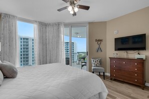 A bedroom with a large bed, a ceiling fan, a TV, and a view of a balcony with a chair. - Palms Resort #1813 Jr. 2BR (Destin)