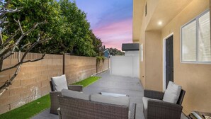 A patio area with wicker furniture, a small lawn, and a view of a building with a door and window. - Cozy Prvate ADU close to Disney Beach EV (Garden Grove)