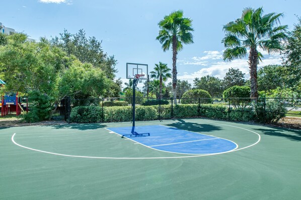 An outdoor basketball court surrounded by trees and a fence.
