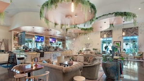 A spacious coffee shop with a modern interior, featuring a bar area, comfortable seating, and a large potted plant. - Palms Resort #1614 Jr. 2BR (Destin)