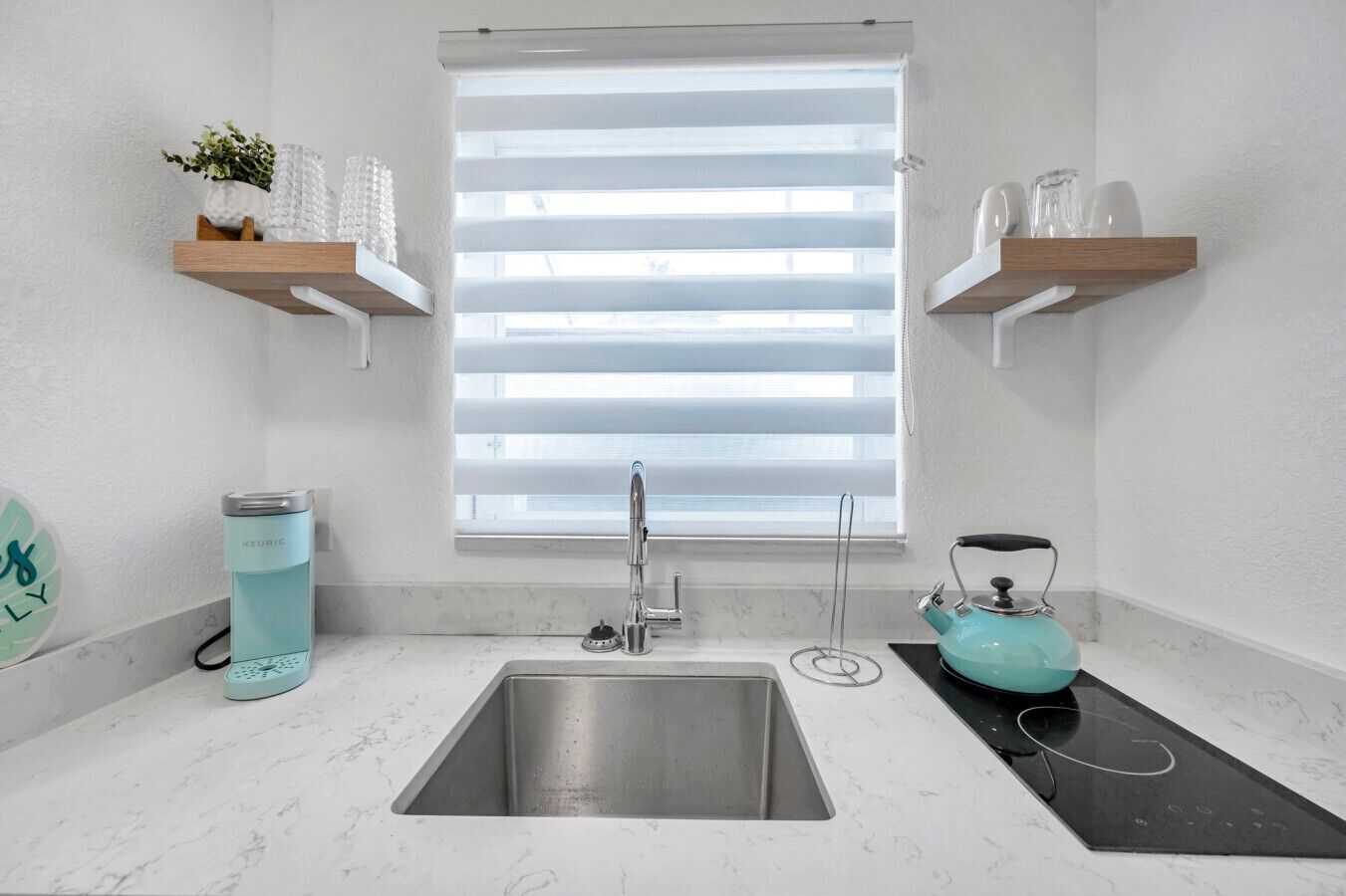 A modern kitchen with a stainless steel sink, a kettle, and a coffee maker on the countertop.