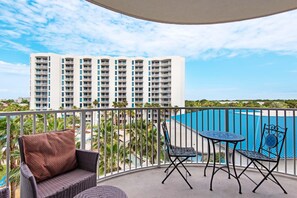 A balcony with wicker furniture, a pool, and a high-rise building in the background.