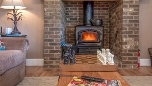 Una sala de estar acogedora con chimenea de ladrillo, repisa de madera y una mesa a cuadros al frente.