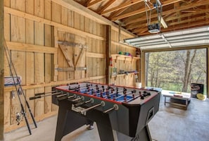 A wooden interior with a foosball table, fishing rods, and a large window offering a view of the outdoors.