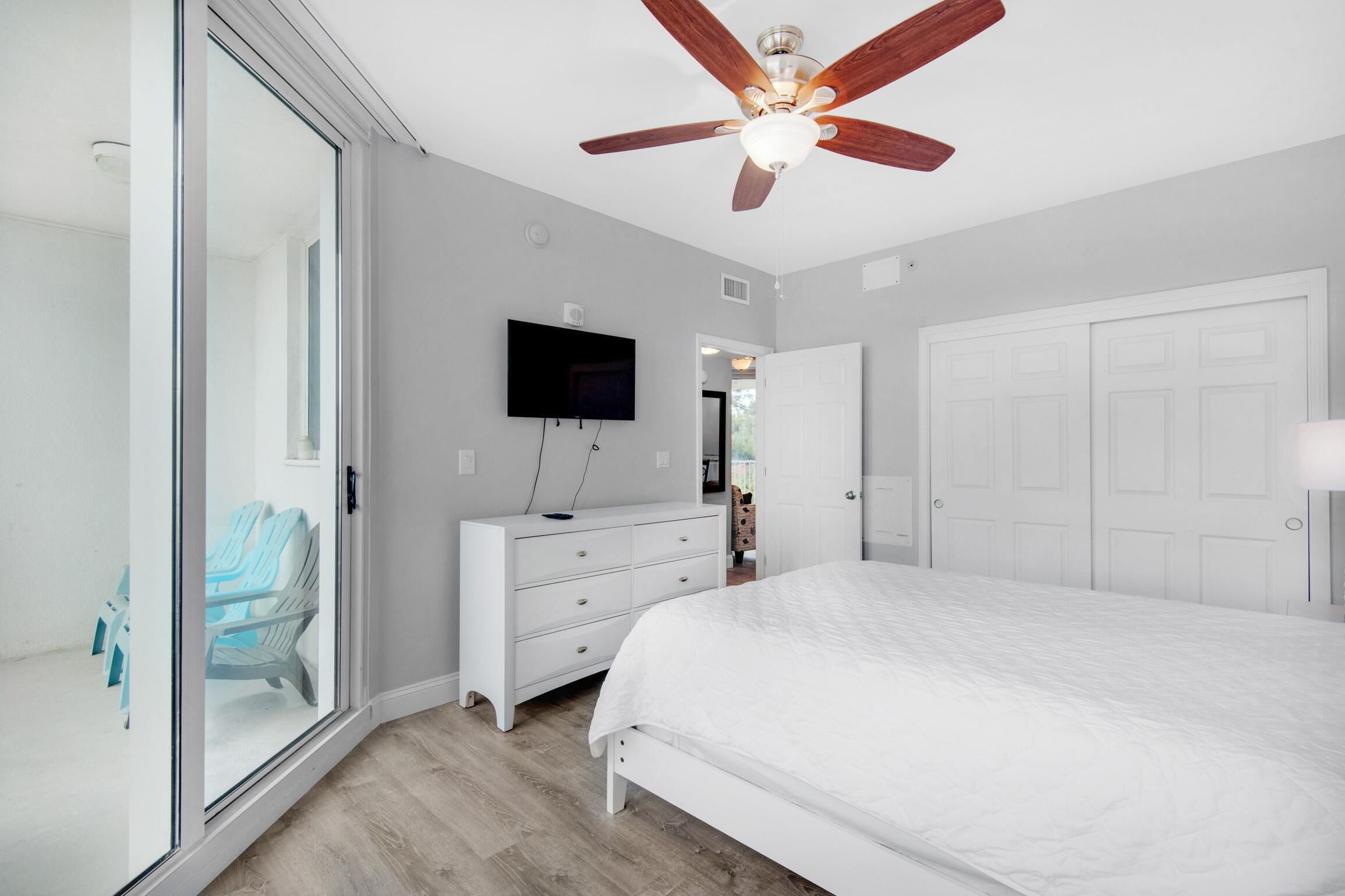 A bedroom with a bed, a dresser, a television, a ceiling fan, and a sliding glass door.