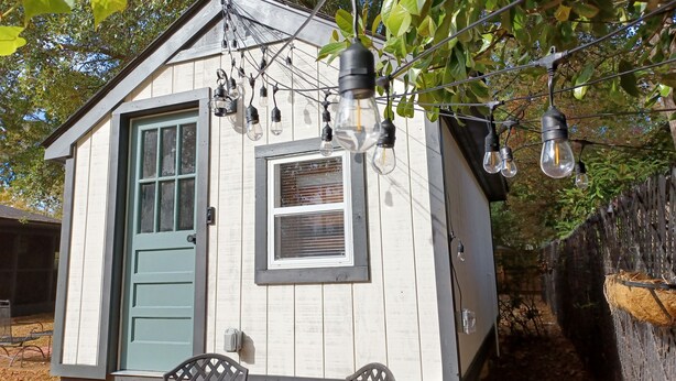 A small wooden cabin with a green door, a window, and a table with chairs. - The Tiny House Experience, at that Treasure House .. 2 bed loft & 1 bath (Smyrna)