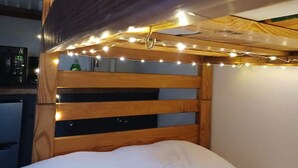 A bunk bed with a wooden headboard and string lights. - The Tiny House Experience, at that Treasure House .. 2 bed loft & 1 bath (Smyrna)