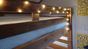 A bunk bed with wooden headboard and railings, string lights, and a yellow floral wall decoration. - The Tiny House Experience, at that Treasure House .. 2 bed loft & 1 bath (Smyrna)