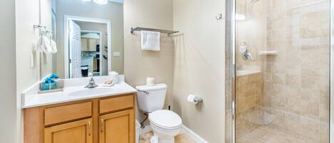 A bathroom with a shower, toilet, sink, and wooden cabinets.