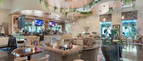 A spacious coffee shop with a modern interior, featuring a bar area, comfortable seating, and a large potted plant.