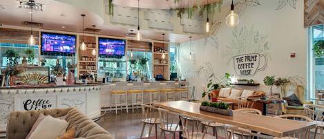 A modern coffee shop interior with a bar area, seating, and decorative plants.
