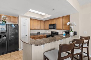 Una cocina moderna con encimeras de granito, armarios de madera, un refrigerador negro, un microondas y una isla central con taburetes de bar.