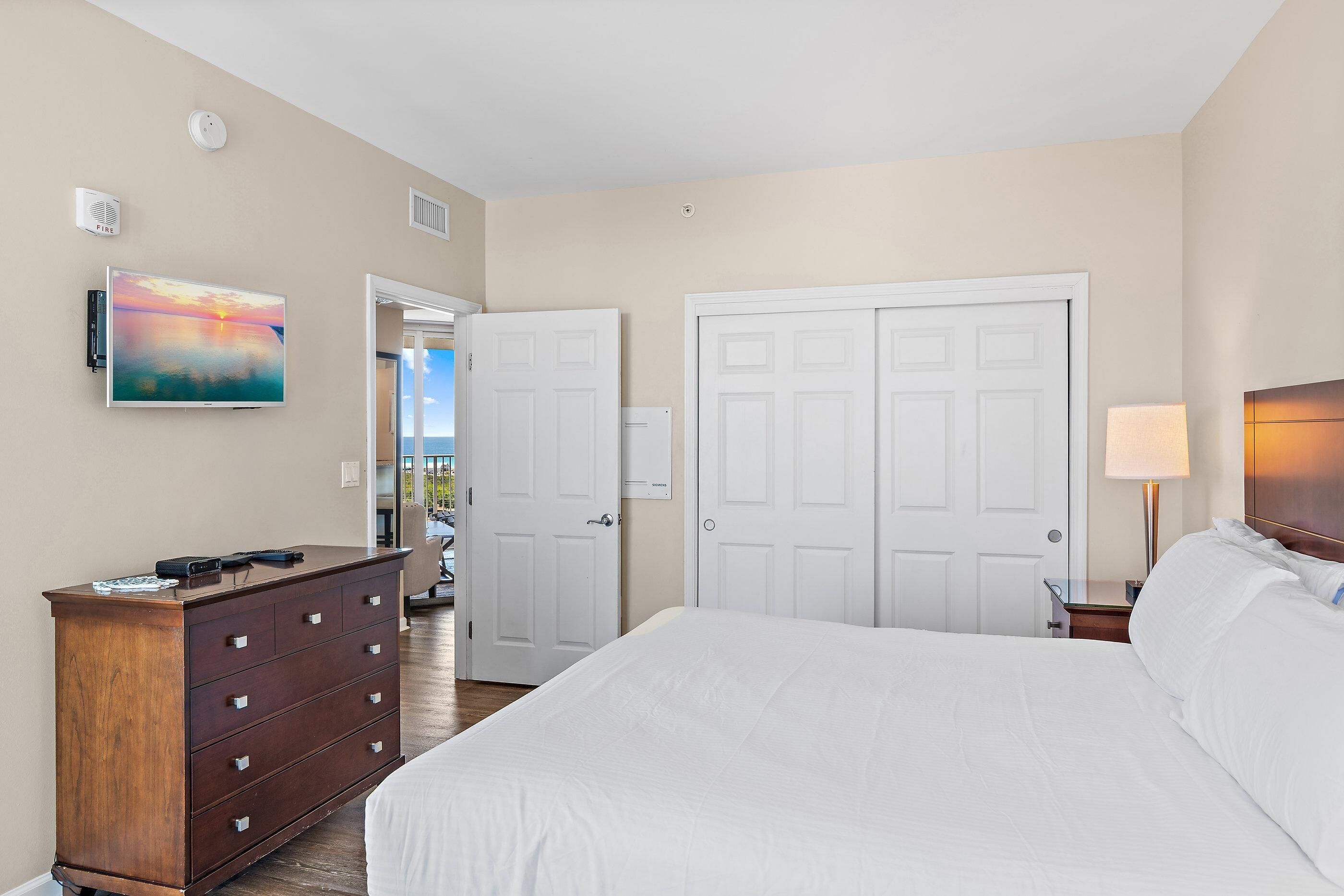 A bedroom with a bed, dresser, two doors, a painting, and a lamp.
