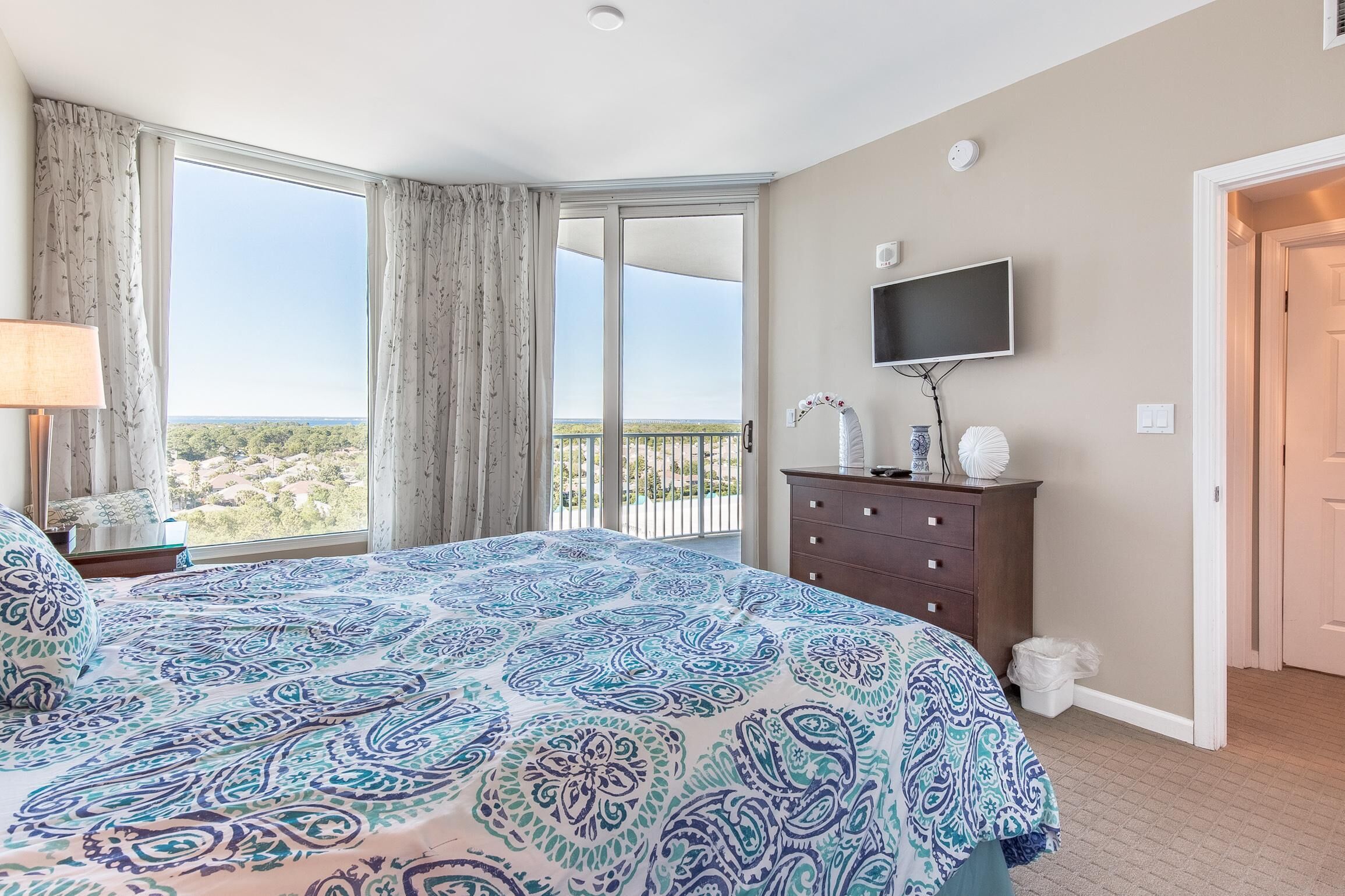 A bedroom with a large bed, a TV, a dresser, and a balcony with a view.
