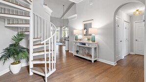 A spacious hallway with a white staircase, a console table with lamps, and a large potted plant. - Thirsty Turtle (Miramar Beach)
