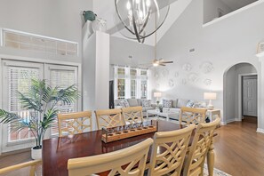 A spacious dining area with a wooden table and chairs, a chandelier, and a large potted plant. - Thirsty Turtle (Miramar Beach)