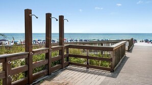 A wooden boardwalk leading to a beach with umbrellas and people. - Thirsty Turtle (Miramar Beach)