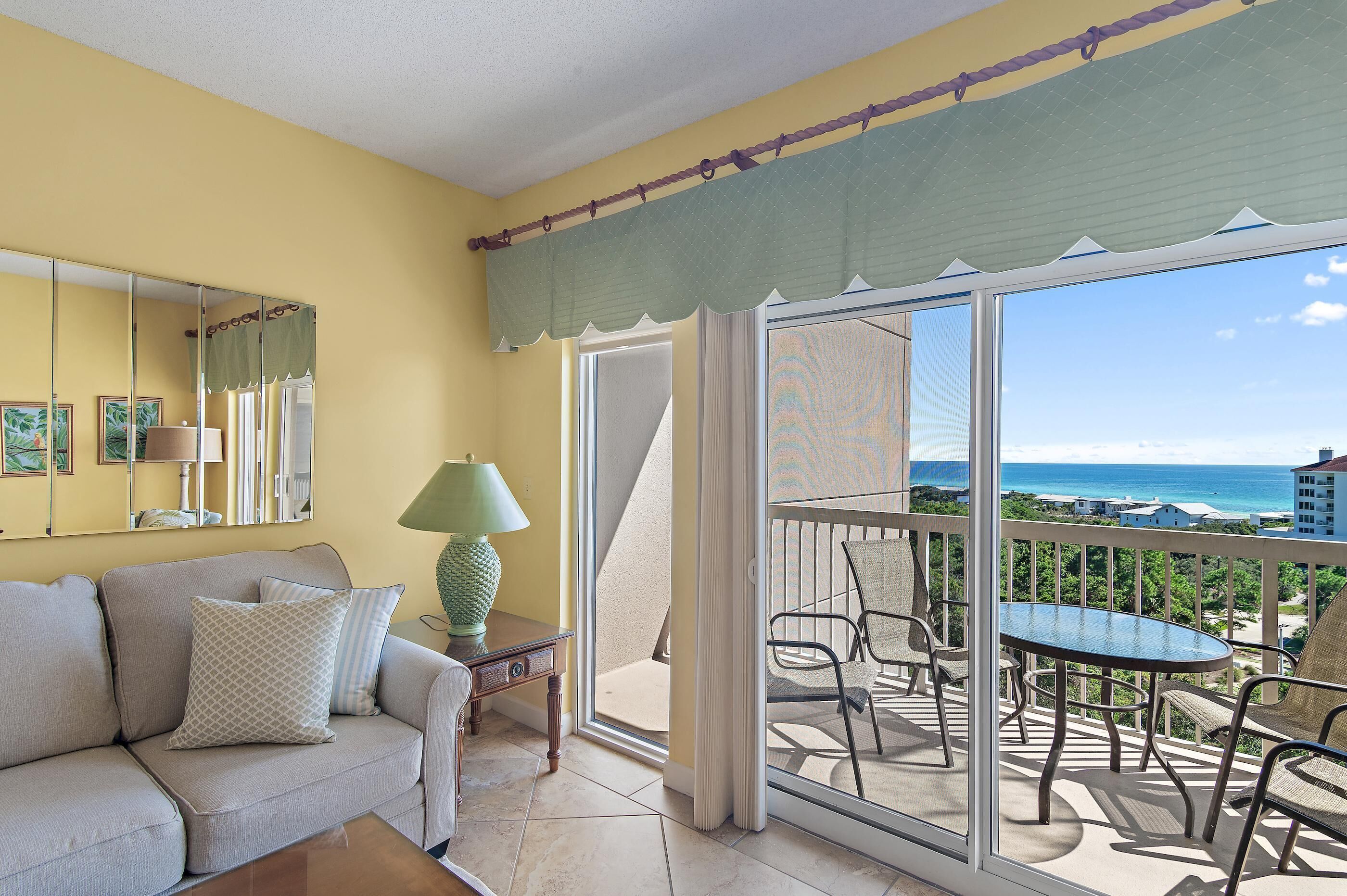A balcony with a view of the ocean, a sofa, a lamp, and a table with chairs.
