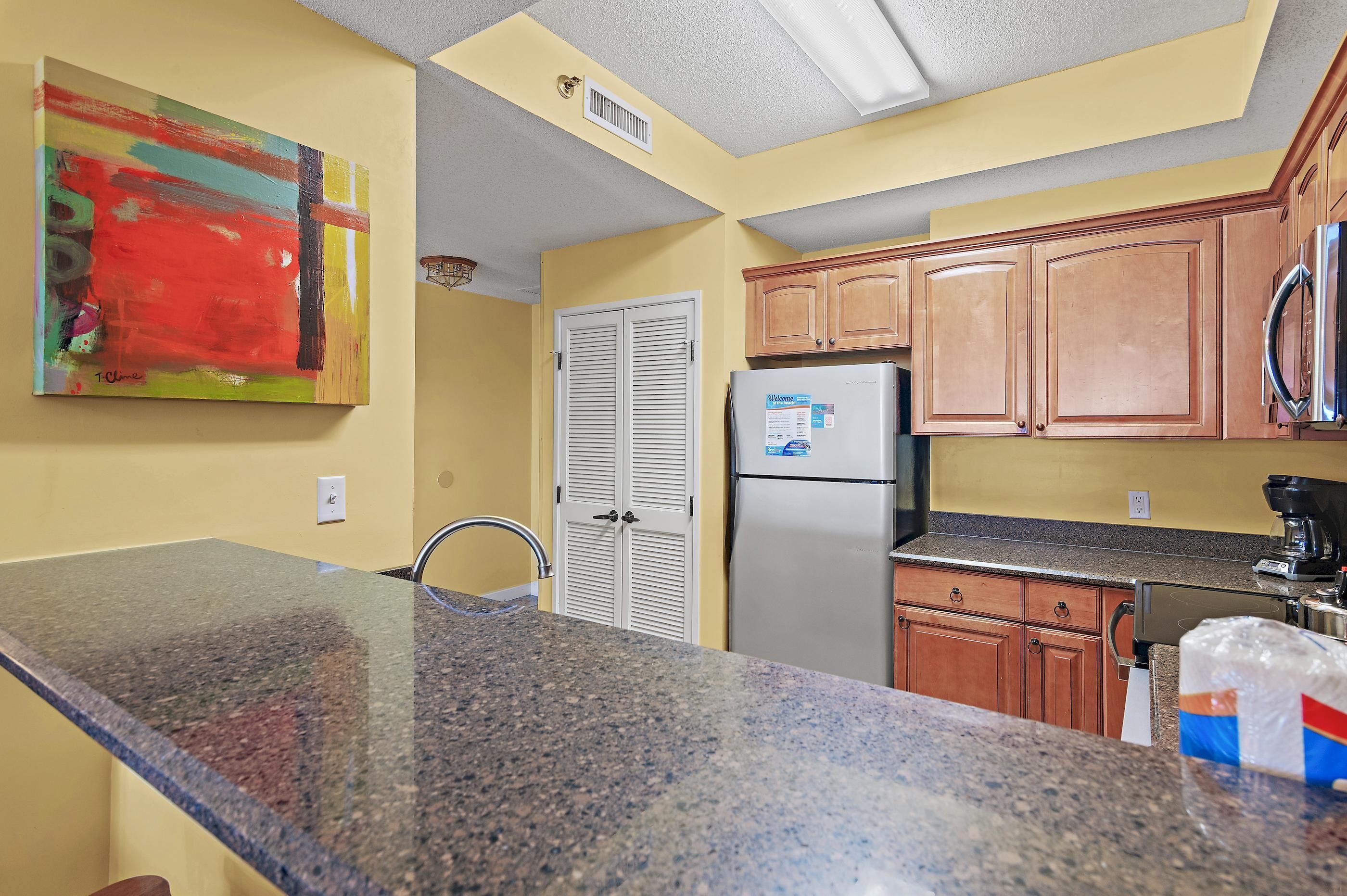 A kitchen with granite countertops, wooden cabinets, a stainless steel refrigerator, and a microwave.
