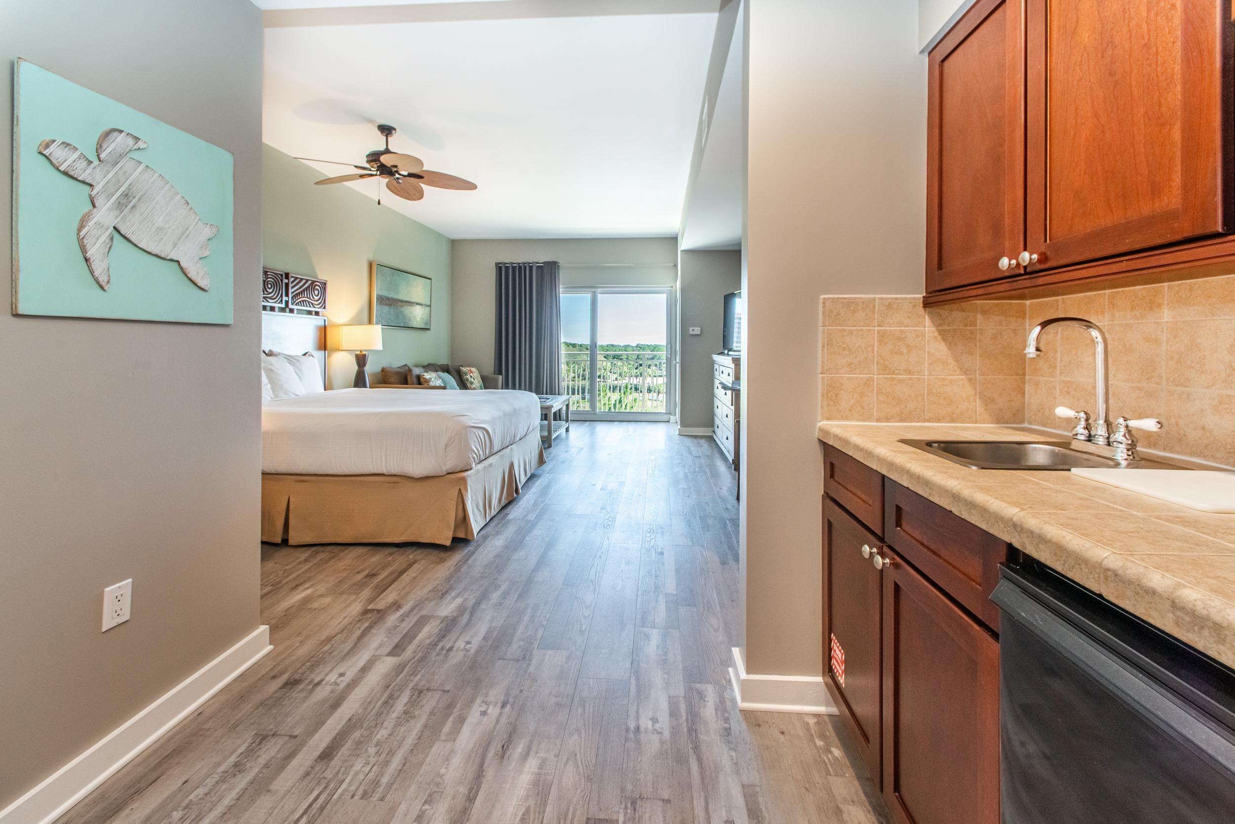 A hotel room with a bed, a ceiling fan, a bathroom with a sink, and a view of the outdoors.