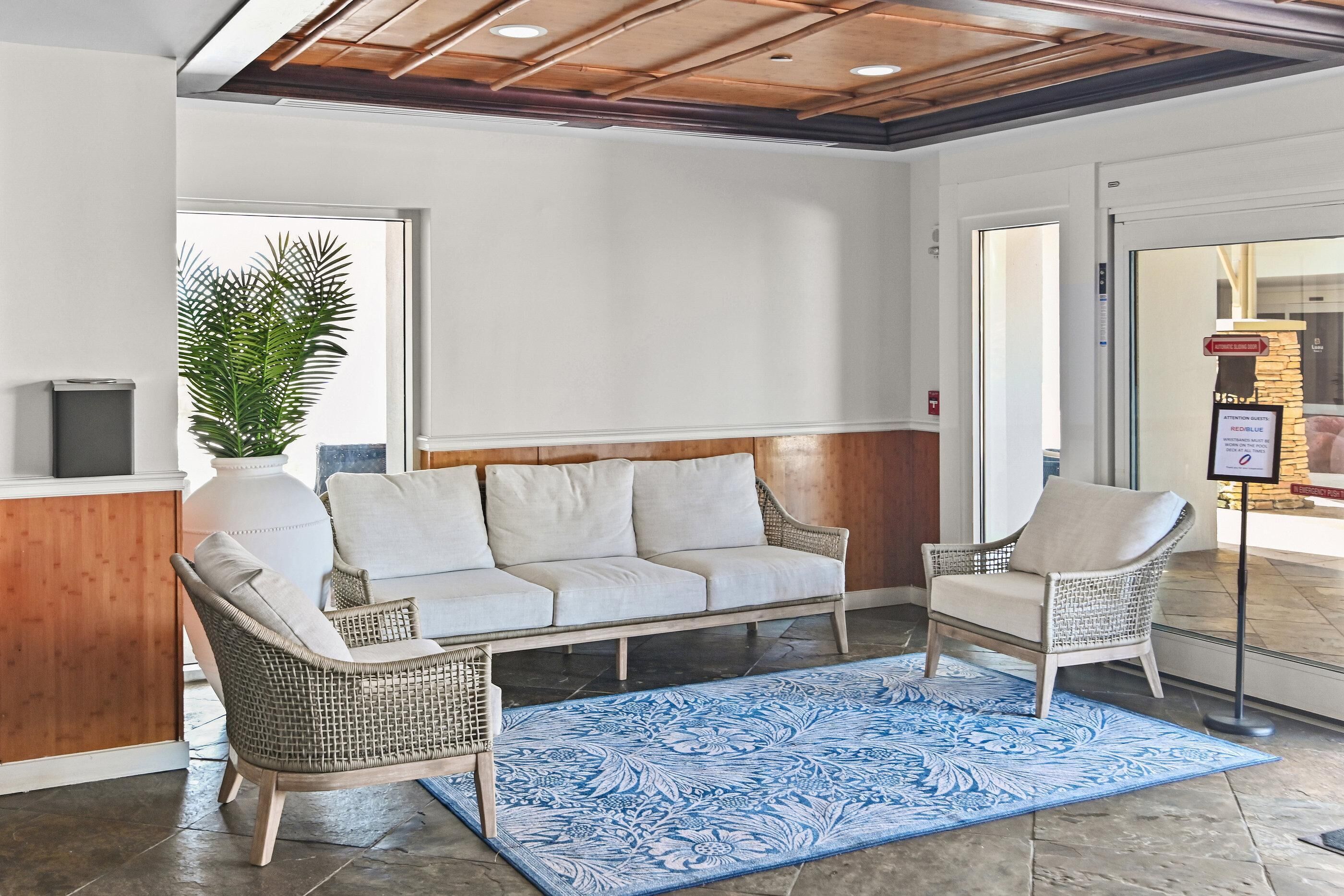 A reception area with a sofa, two wicker chairs, a potted plant, and a blue patterned rug.