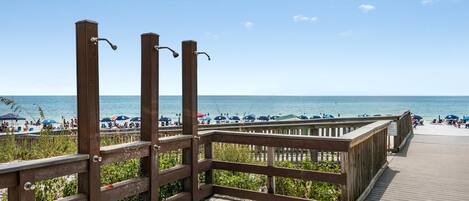 A wooden boardwalk leading to a beach with umbrellas and people.