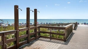 A wooden boardwalk leading to a beach with umbrellas and people.