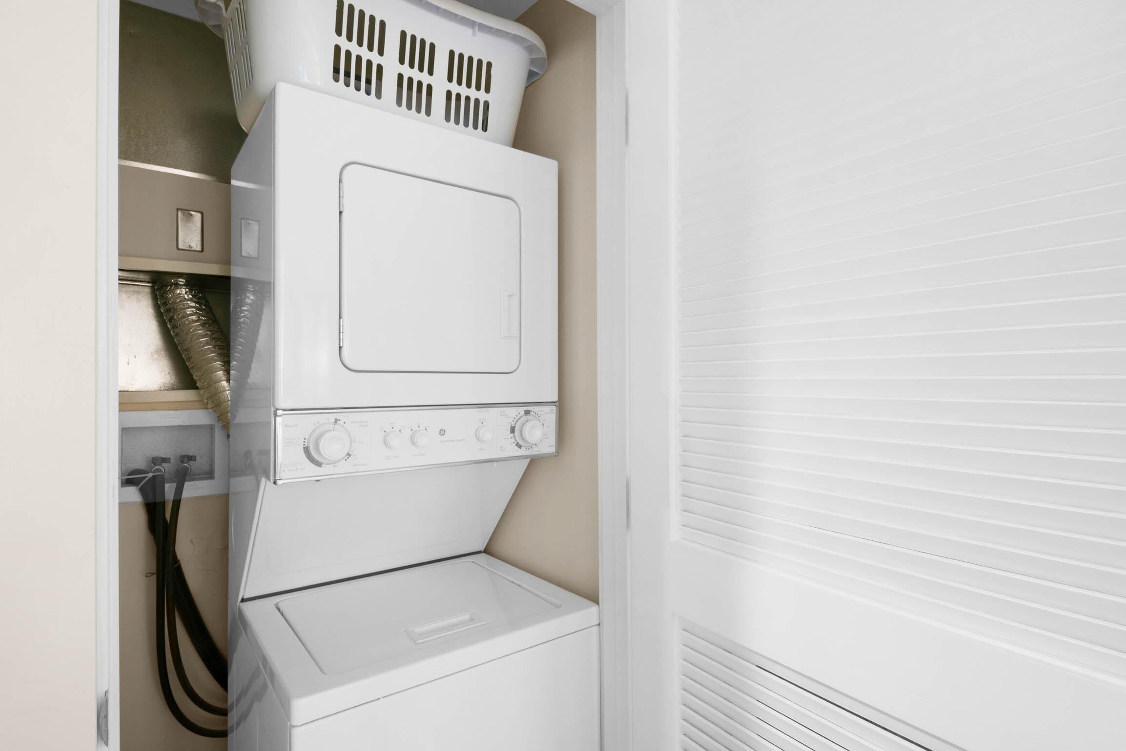 A stacked washer and dryer unit in a laundry room with a white door and a vent hose visible.