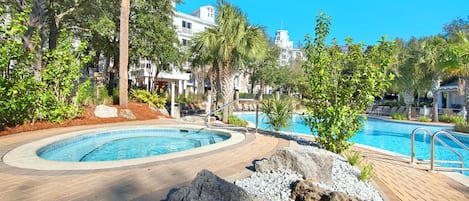 Un área de piscina con jacuzzi, rodeada de palmeras y un camino de ladrillo.
