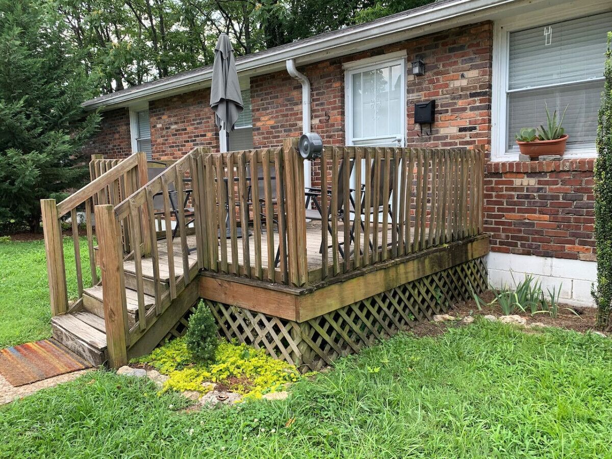 A residential house with a wooden deck, a brick exterior, and a small garden area with yellow flowers.