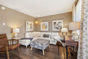 Ein modernes Wohnzimmer mit einer Eckcouch, einem Holztisch und einem kleinen Beistelltisch mit einer Lampe.