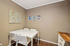Ein kleines, sauberes Zimmer mit einem weißen Tisch und Stühlen, einer Holzeinrichtung und drei gerahmten Bildern an der Wand.
